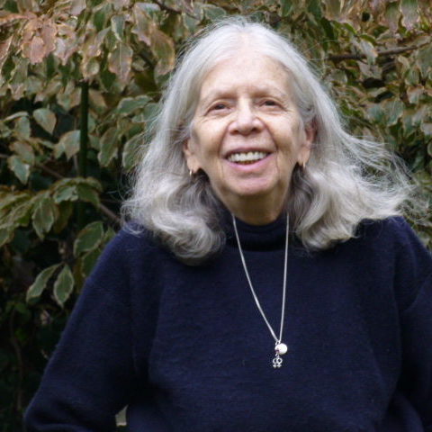 Headshot of a lesbian outdoors with green shrubbery for a backdrop.