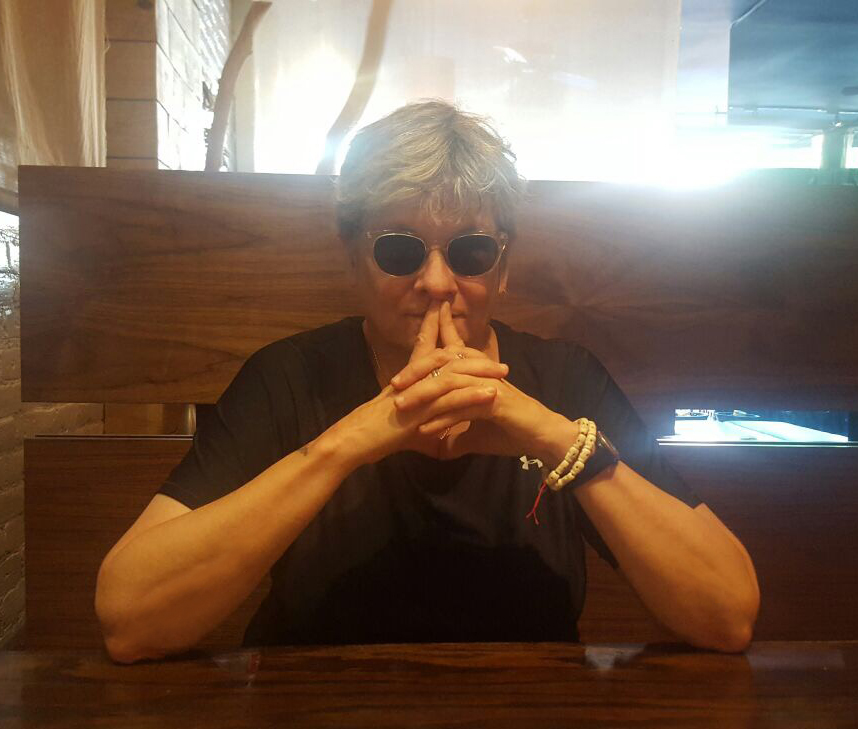 Headshot of a lesbian sitting at a table wearing sunglasses.