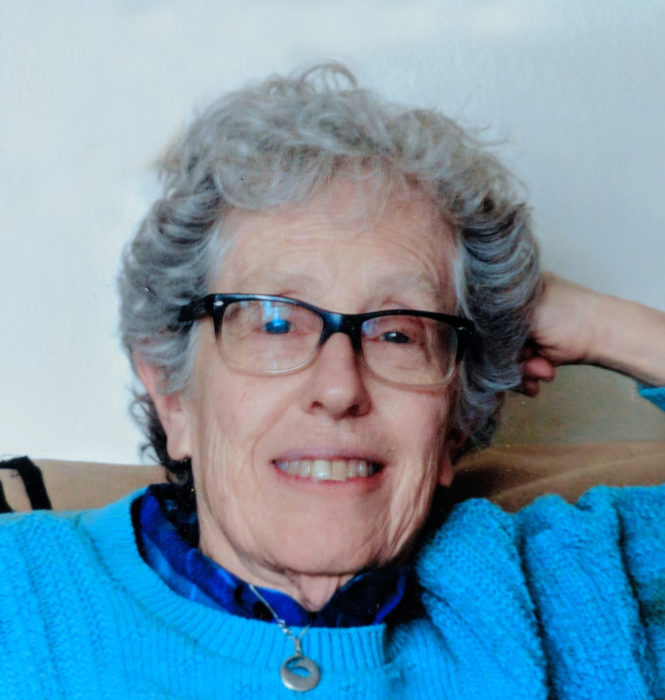 Headshot of a lesbian in a blue sweater sitting with her head resting against one hand.