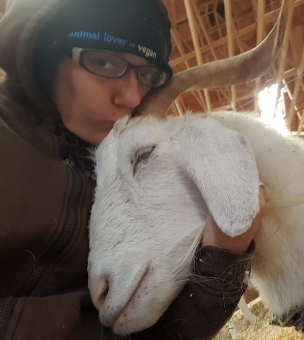 Headshot of a lesbian kissing a goat on the head.
