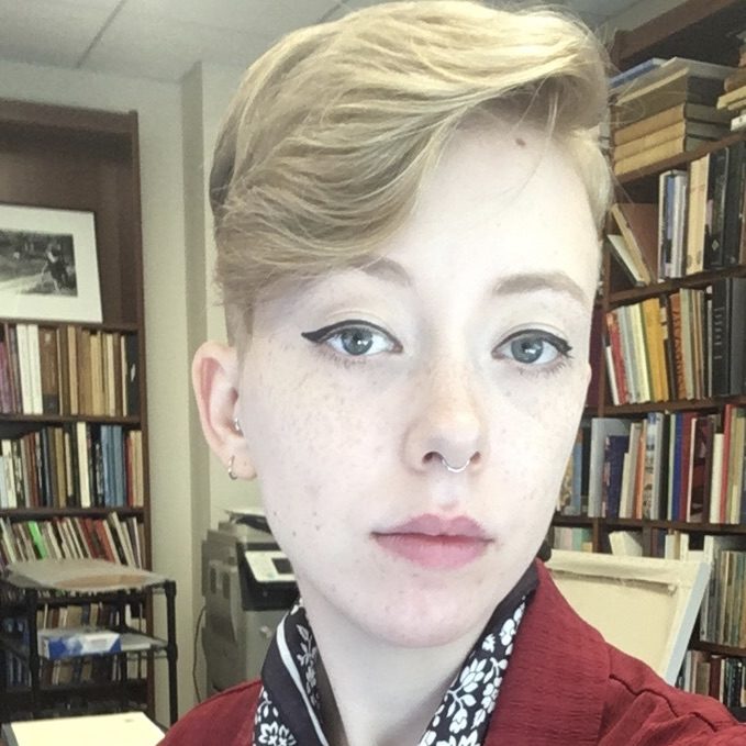 Headshot of a lesbian in a room lined with bookshelves.